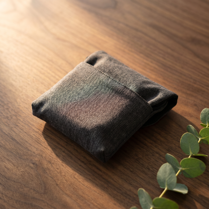 NeckReset Pro folded into compact travel pouch on warm walnut surface with eucalyptus